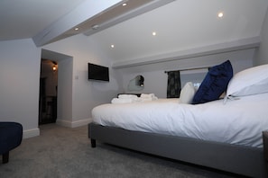 A modern bedroom with a large bed, a flat-screen TV, and a ceiling-mounted light fixture. - Braithwaite House Rooms (Keswick)