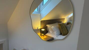 Ein Schlafzimmer mit einem Bett, einem Nachttisch, einer Lampe und einem an der Wand befestigten Spiegel.