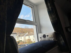 Una habitación con ventana que da a una zona residencial, una cama con colchón azul y un almohadón con diseño de oveja.
