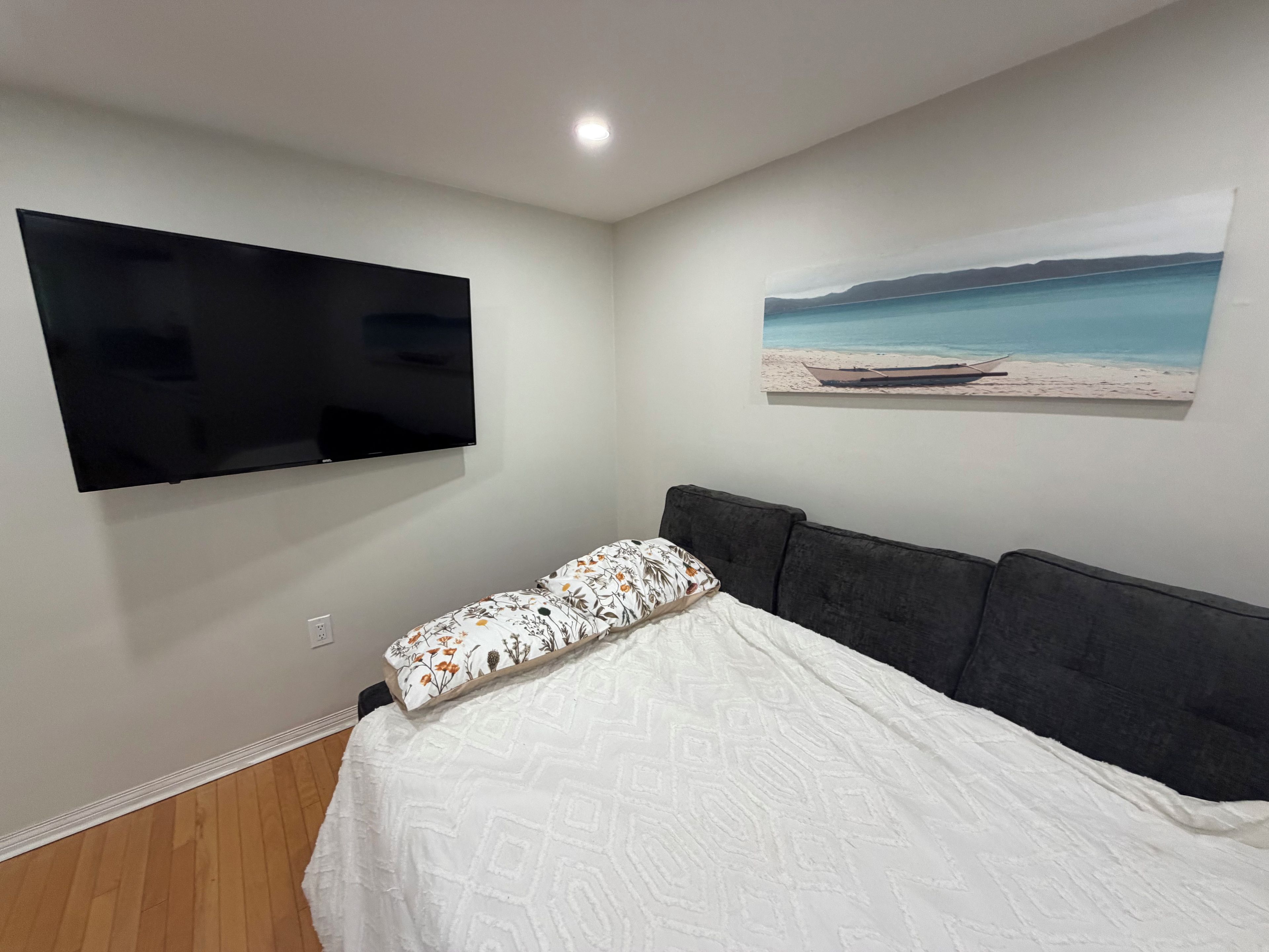 Un dormitorio con una cama, un televisor de pantalla plana montado en la pared y un cuadro con una escena de playa.