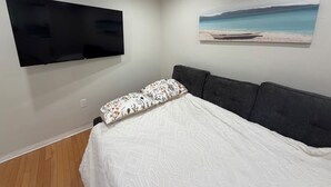 Une chambre à coucher avec un lit, un téléviseur à écran plat fixé au mur et un tableau représentant une scène de plage.