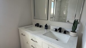 Une salle de bain avec un meuble-lavabo à deux vasques, un grand miroir et une plante en pot.
