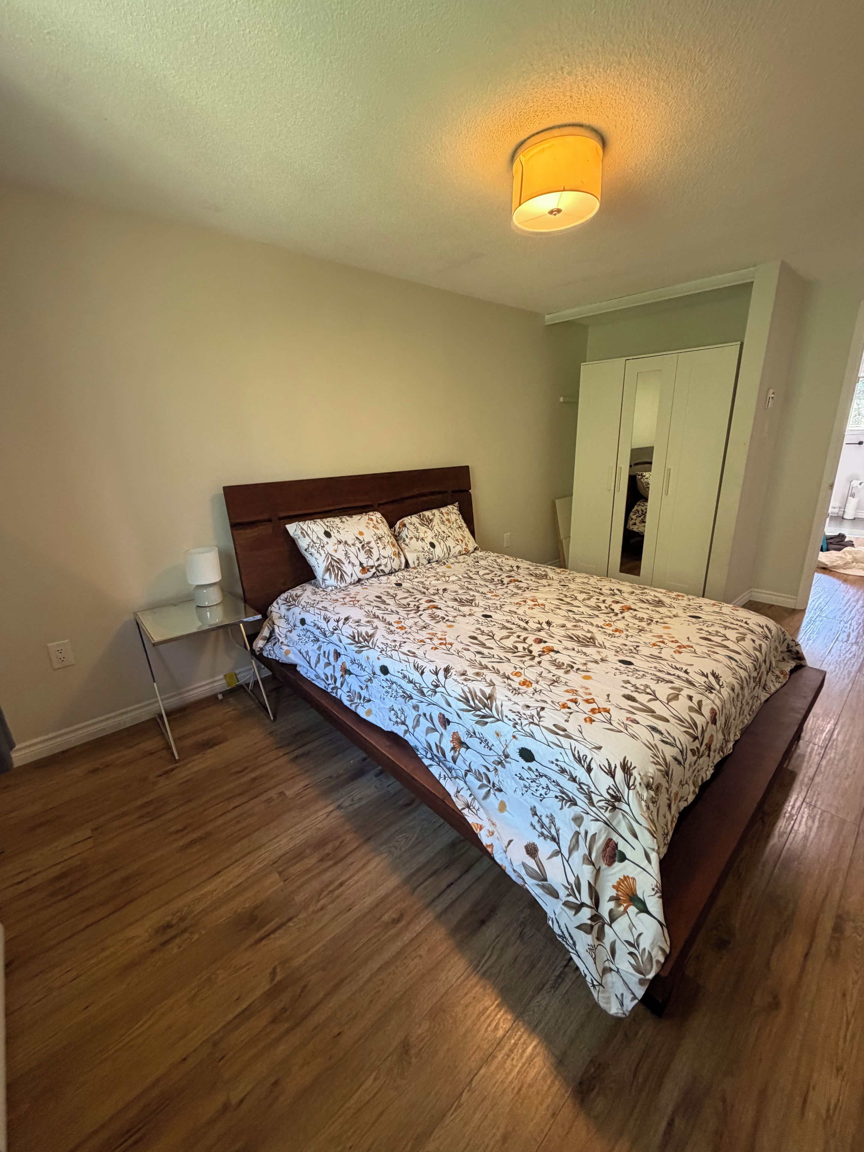 Une chambre à coucher avec un lit en bois, une table de chevet, une armoire et un luminaire au plafond.