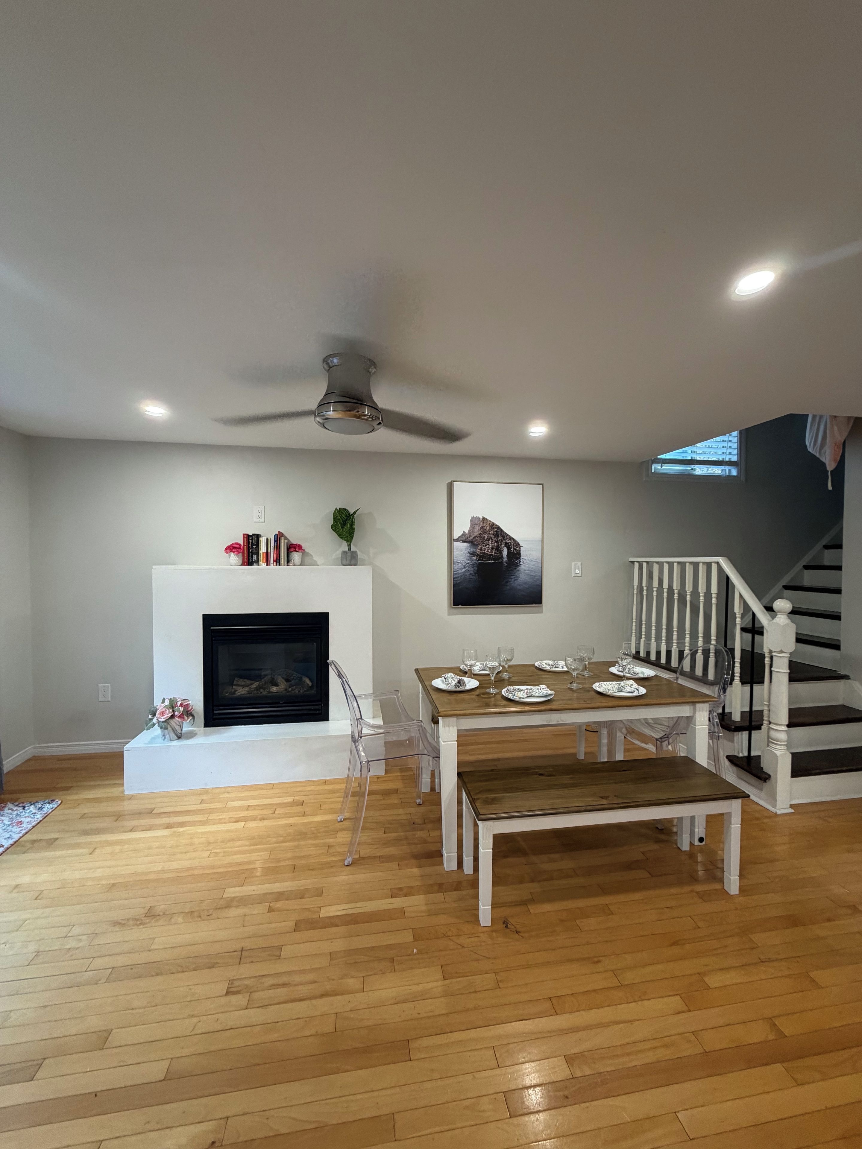 Amplia sala de estar con chimenea, una mesa de comedor para cuatro personas y una escalera que sube a un nivel superior.