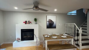 Un salon spacieux avec une cheminée, une table à manger dressée pour quatre personnes et un escalier menant à l’étage supérieur.