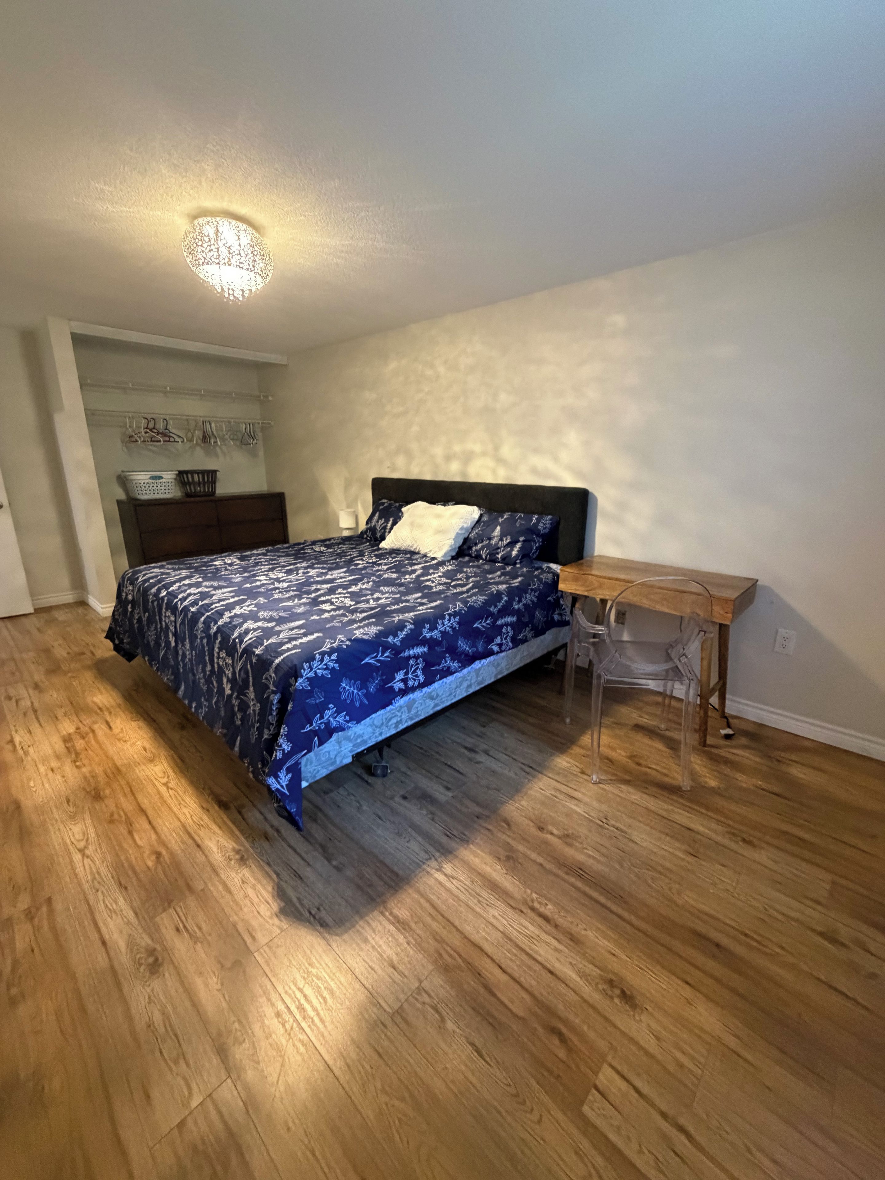 A bedroom with a bed, wooden flooring, a nightstand, and a chair.