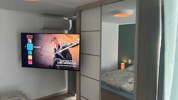 A modern bedroom with a TV mounted on the wall displaying a movie, a bed with floral bedding, and a bedside table.