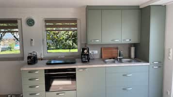 A modern kitchen with light green cabinets, a built-in oven, a coffee maker, and a window with a view of greenery.