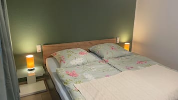 Ein Bett mit floralem Bettzeug, ein Holzkopfteil, Nachttischlampen und ein Nachttischchen mit Lampe.