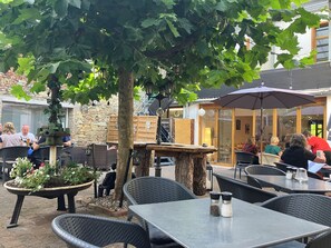 An outdoor seating area with tables and chairs, surrounded by greenery and a stone wall.