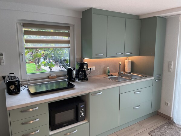 A modern kitchen with a built-in microwave, a coffee maker, and a window with blinds.