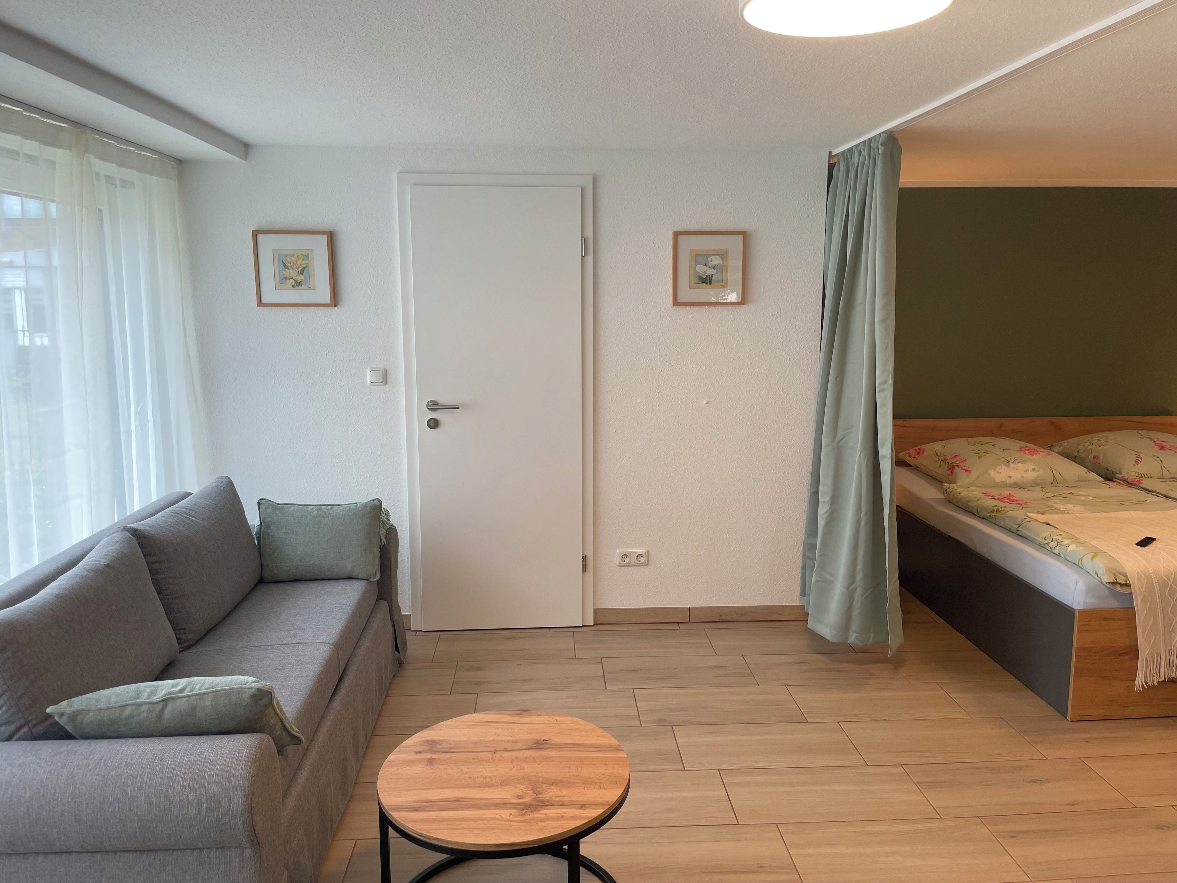 Ein Zimmer mit einer Couch, einem kleinen runden Tisch, einem Bett mit Blumenmuster und zwei gerahmten Bildern an der Wand.