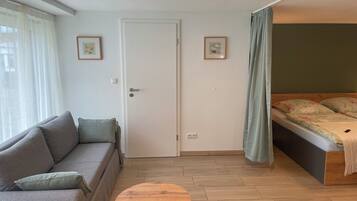 Ein Zimmer mit einer Couch, einem kleinen runden Tisch, einem Bett mit Blumenmuster und zwei gerahmten Bildern an der Wand.