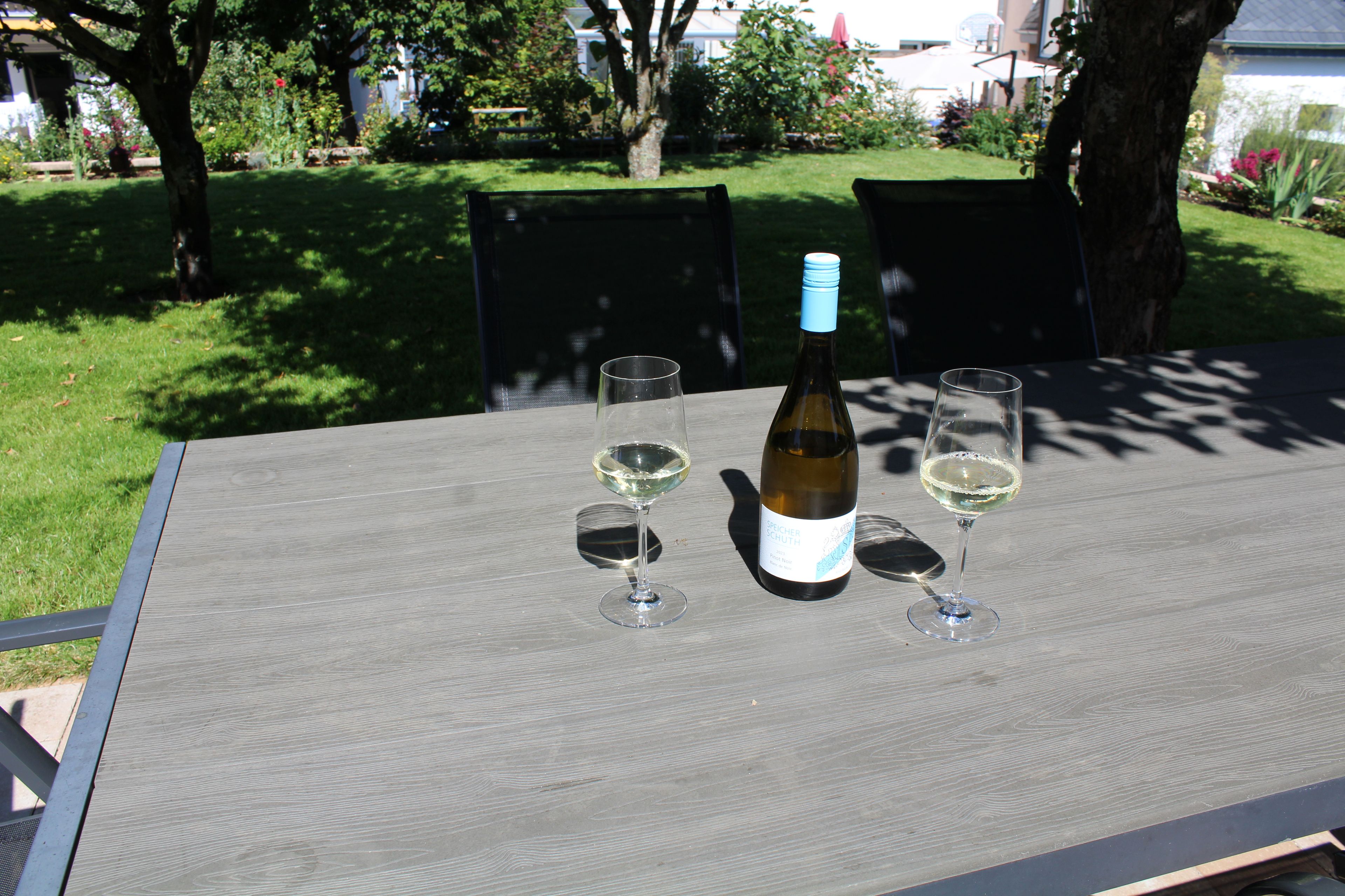 Ein Tisch mit einer Flasche und zwei Gläsern, draußen im Garten platziert.