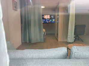 Ein Wohnzimmer mit einem grauen Sofa, einem Fernseher der einen Film zeigt und einem Holzboden.