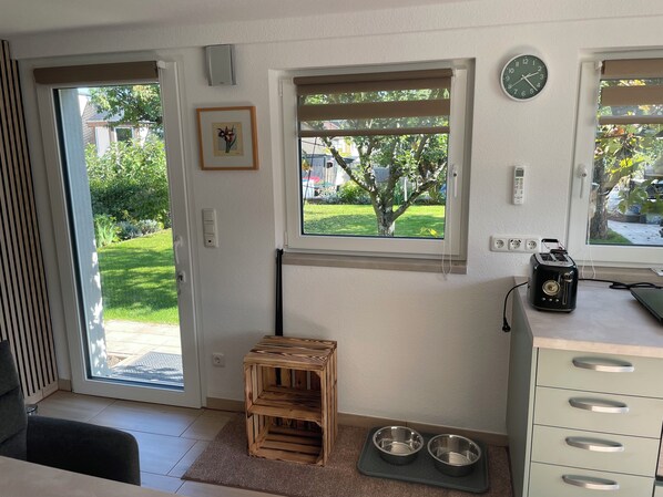 A room with a sliding glass door, a small wooden stool, a pet feeding station, and a toaster on the counter.