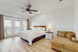 A hotel room with a bed, a nightstand, a chair, a ceiling fan, and a balcony with a view. - Beach Estate (Gulf Shores)