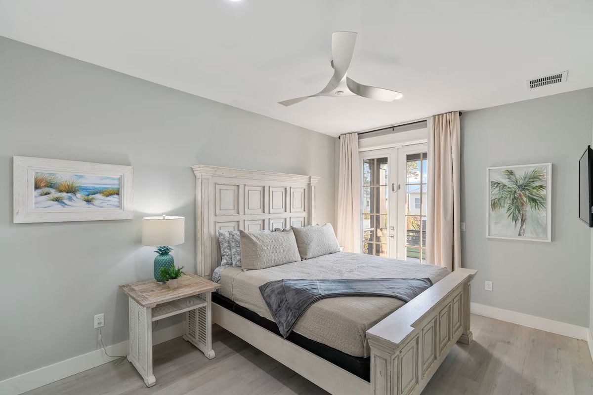 Quarto com cama, mesa de cabeceira, ventilador de teto e obras de arte nas paredes.