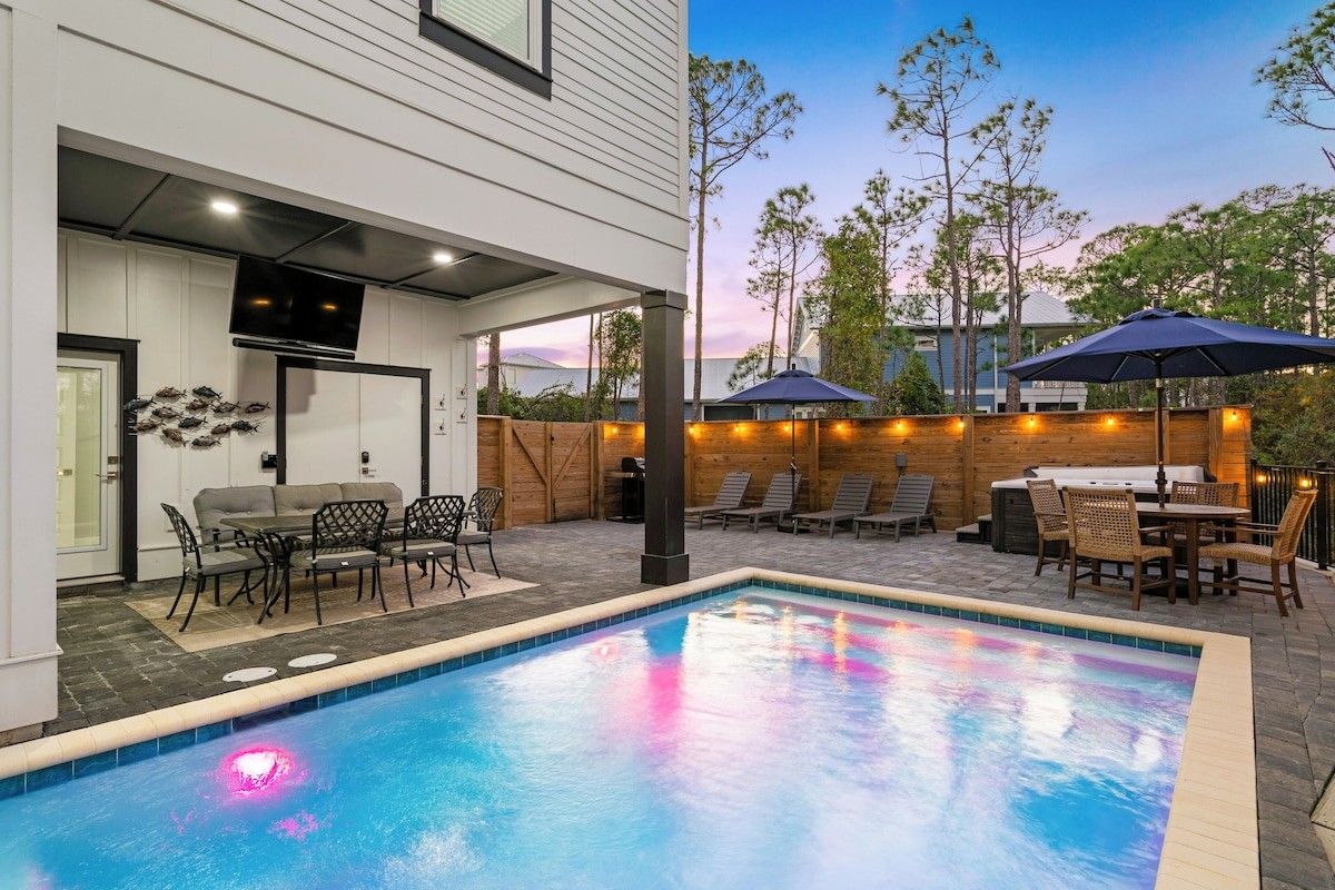 A swimming pool with a patio area, outdoor furniture, and a barbecue setup.