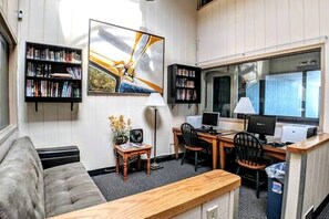 A compact living space with a sofa, a desk with two computers, a bookshelf, and a window.