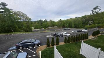 Un parking avec plusieurs voitures et une zone délimitée par une clôture, où se trouvent des arbres.
