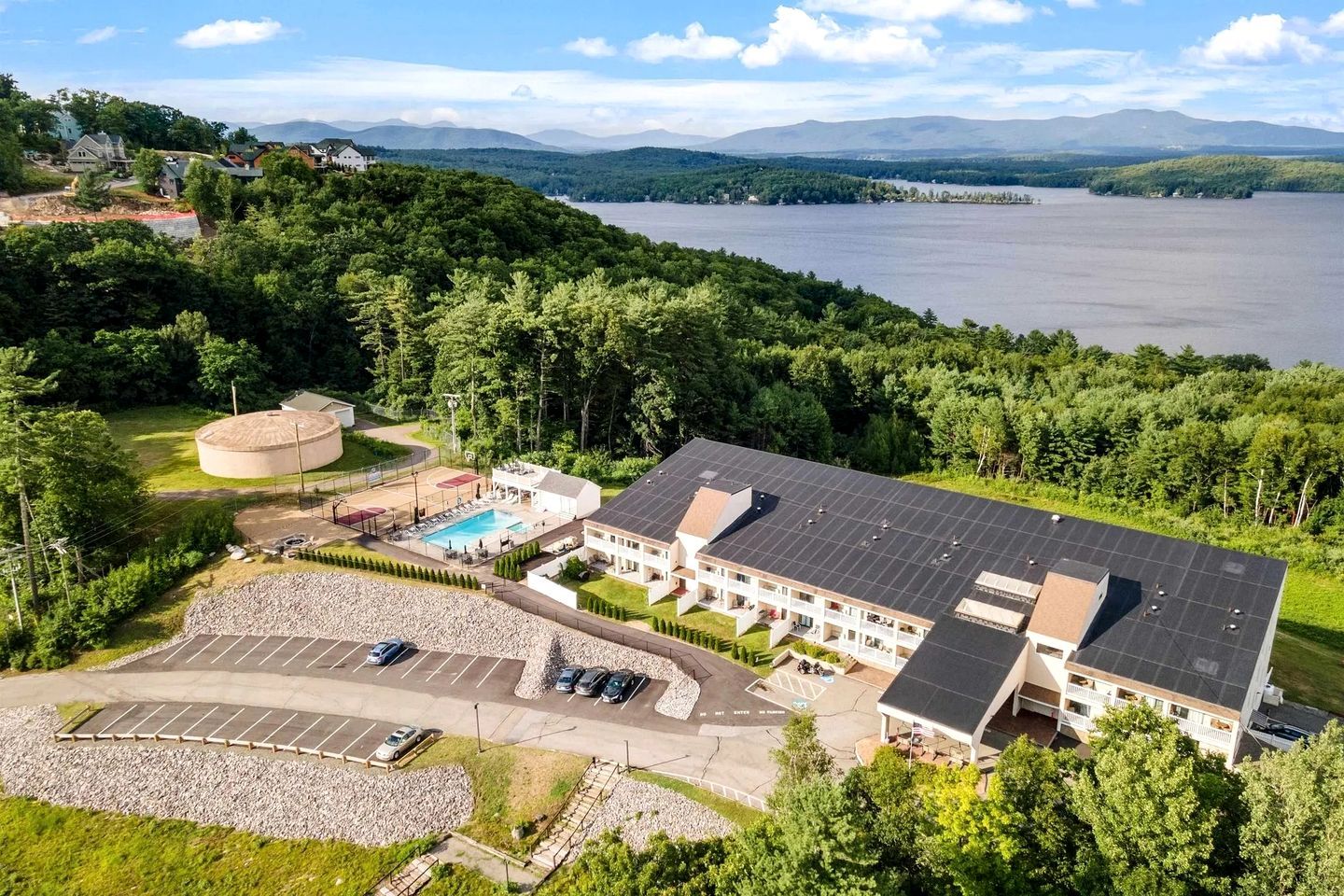 Ein Hotel mit Swimmingpool, Parkplatz und Blick auf einen See und Berge.