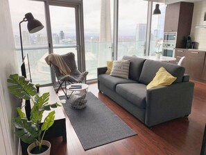 A modern living room with a grey sofa, a small table, and a potted plant. - Elegant & Spacious 2BR1BA Downtown Condo w/Parking (Toronto)