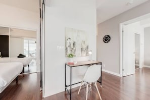 A modern hotel room with a bed, a desk with a chair, a wall clock, and a cityscape artwork. - Elegant & Spacious 2BR1BA Downtown Condo w/Parking (Toronto)