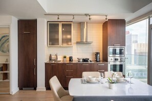 A modern kitchen with dark wood cabinets, a white countertop, and a dining area with a table set for two. - 1BR Condo with City View, Near CN Tower & Parking (Toronto)