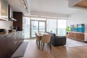 A modern kitchen with a dining area, large windows, and a flat-screen TV. - 1BR Condo with City View, Near CN Tower & Parking (Toronto)