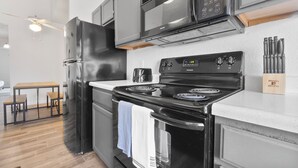 A modern kitchen with a black refrigerator, stainless steel microwave, and a black stove. There is a wooden table with chairs and a ceiling fan. - Cozy Gainesville Apt • 2BR 2BA Stay near UF Campus (Gainesville)