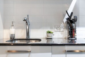 A modern kitchen with a stainless steel sink, a faucet, a soap dispenser, a small potted plant, and a utensil holder. - Stylish 1BR APT near DWTN with Balcony Views (Toronto)