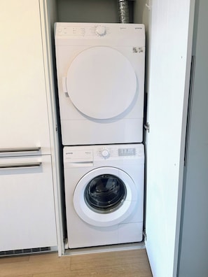 Un appareil compact, composé d’une laveuse à chargement frontal et d’une sécheuse à chargement par le haut, le tout intégré dans un espace étroit doté d’un plancher en bois.