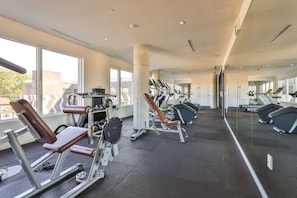 Une salle de sport moderne équipée de machines de cardio, de postes d’entraînement avec poids et bénéficiant d’un éclairage naturel abondant.