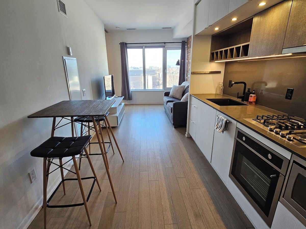 A compact kitchen with a dining area, a sofa, and a view through a large window.