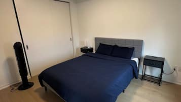Un dormitorio con cama, mesitas de noche, un ventilador y una puerta.