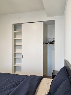 Une chambre à coucher avec un lit, une armoire avec des étagères et une tringle pour suspendre les vêtements.