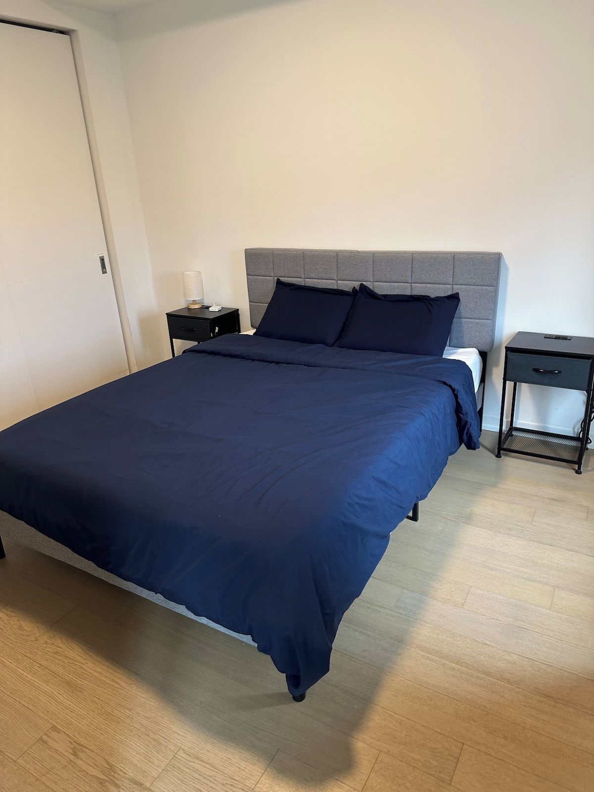 A bedroom with a large bed, a nightstand, a drawer, and a door.