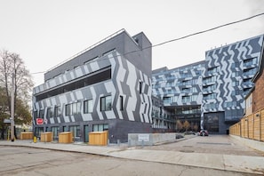 Un bâtiment moderne à la façade ornée d’un motif en zigzag, un panneau de signalisation indiquant un arrêt obligatoire et une aire de stationnement avec une voiture.