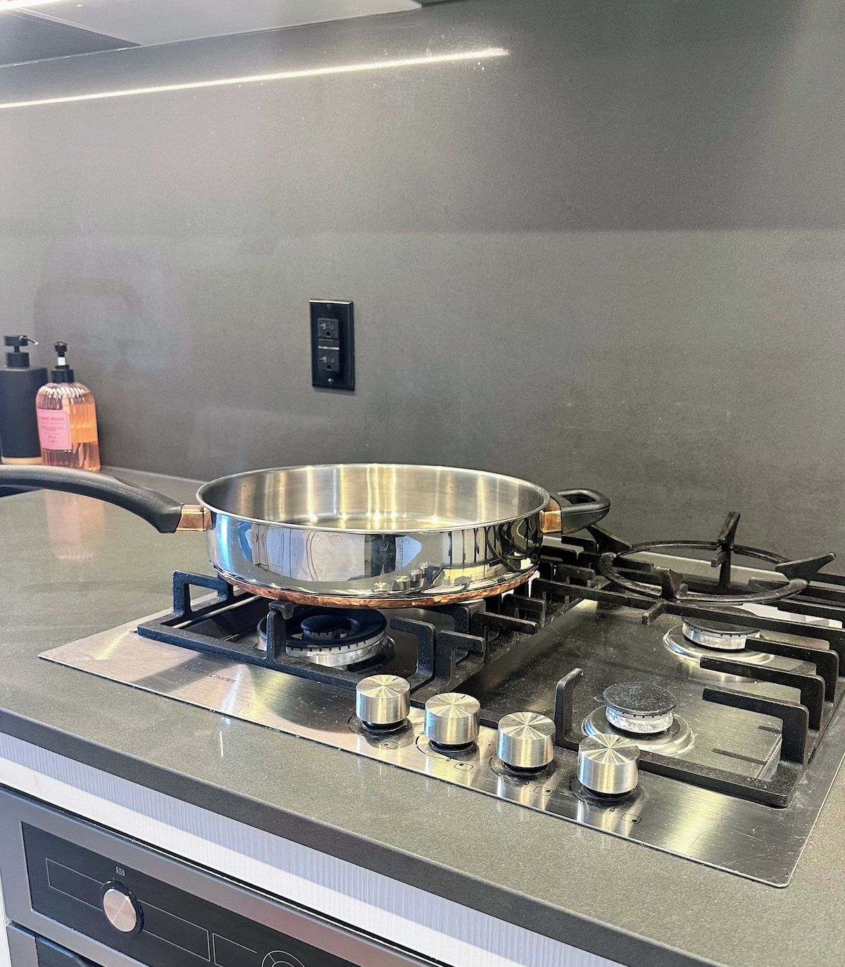A kitchen with a stainless steel stove, a pot on the burner, and a soap dispenser on the counter.