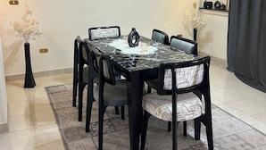Een eetgedeelte met een marmeren tafel, zwarte stoelen met gestreepte kussens, een vaas met gedroogde bloemen en een lijstwerkkunstwerk aan de muur.