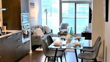 A modern kitchen with dark cabinetry, a dining area with a glass table, and a large window providing a view of the city.