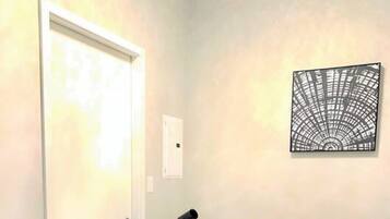A neatly made bed with a rolled towel and a small plant, a bedside lamp, and a wall art piece.