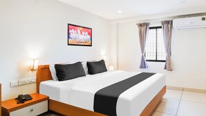 Quarto de hotel com uma cama grande, mesas de cabeceira, um quadro, janela com cortinas e ar condicionado.