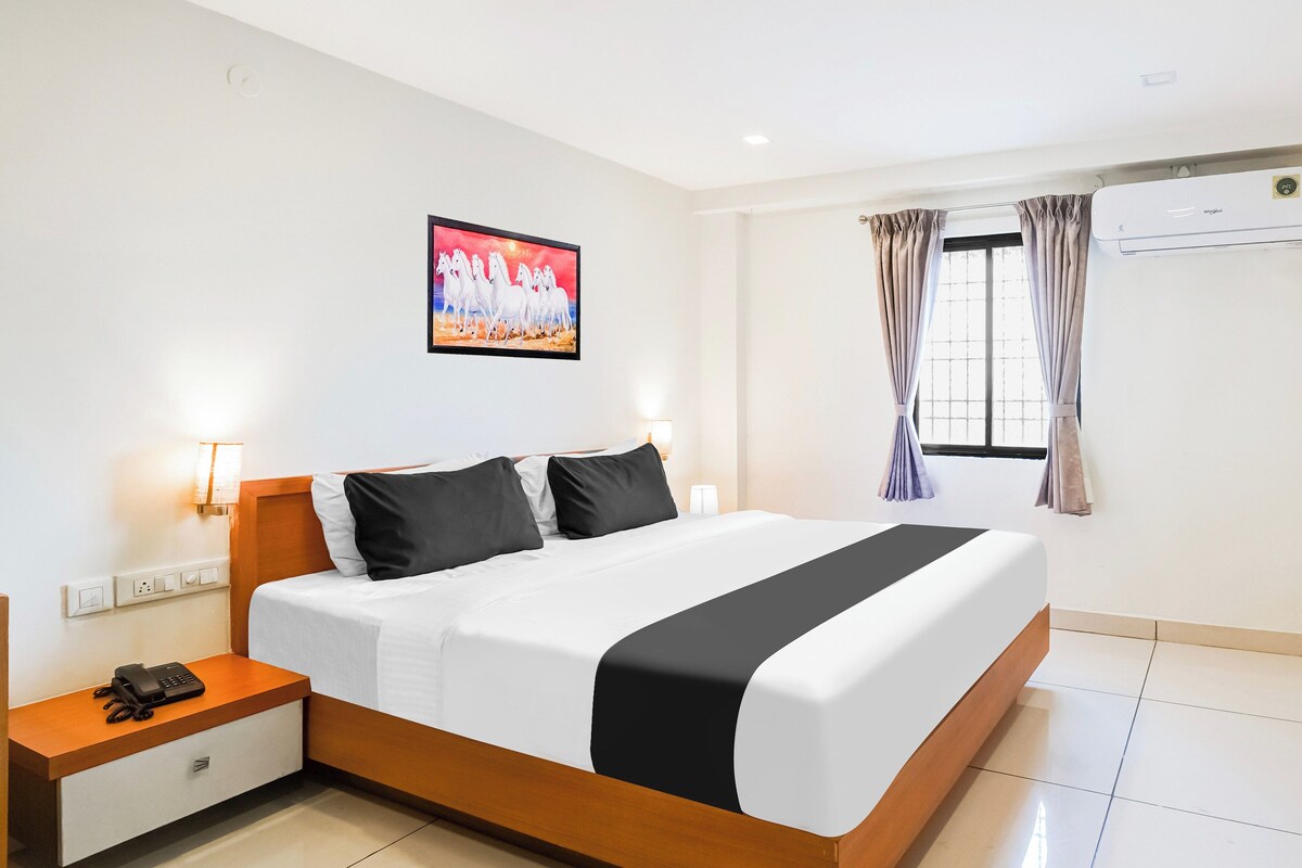 Una habitación de hotel con una cama grande, mesitas de noche, un cuadro, una ventana con cortinas y un equipo de aire acondicionado.