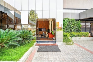 A modern building entrance with a reception desk, seating area, and a view of the surrounding greenery.