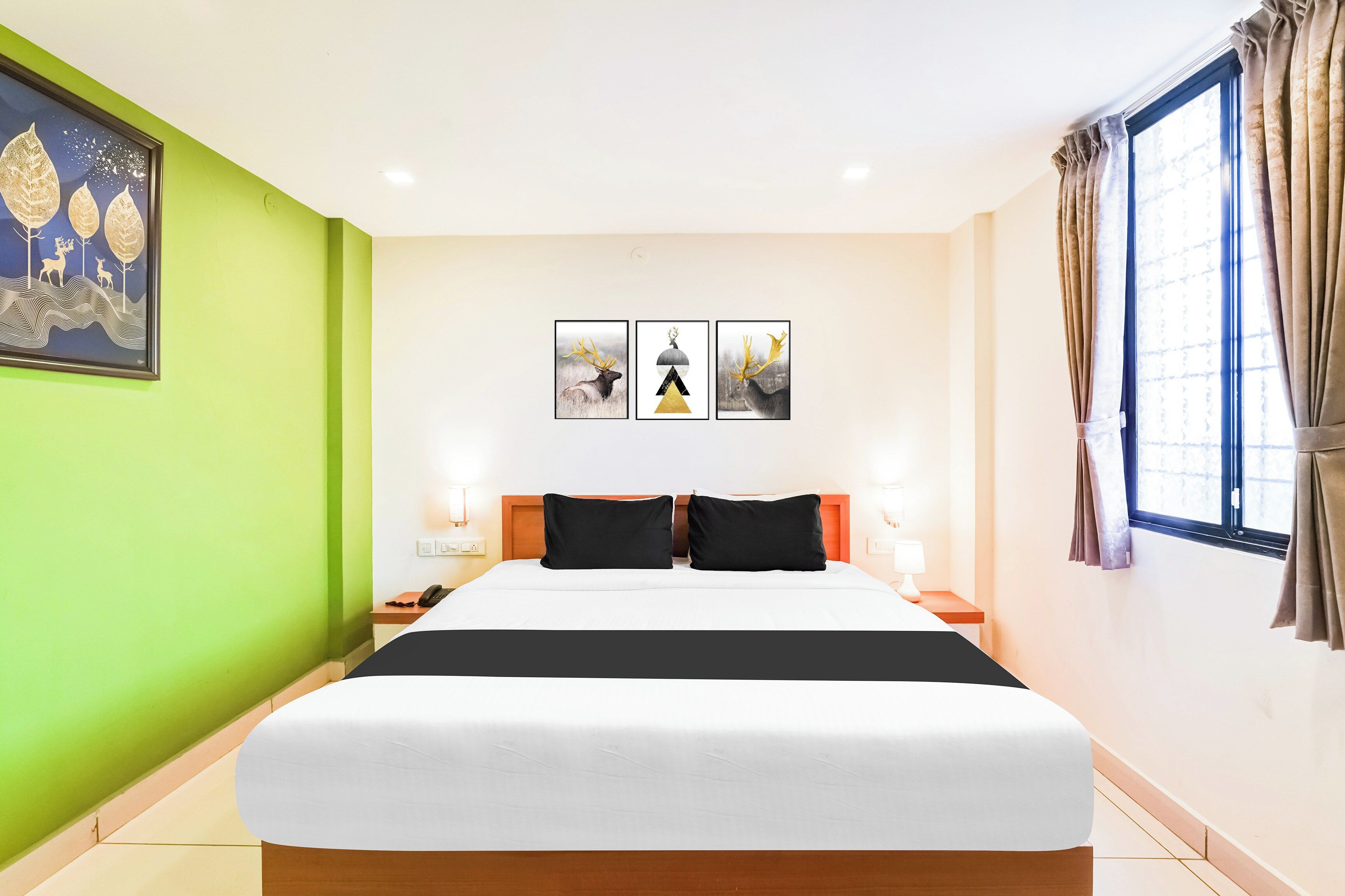 A hotel room with a large bed, a green accent wall, and three framed pictures above the bed.