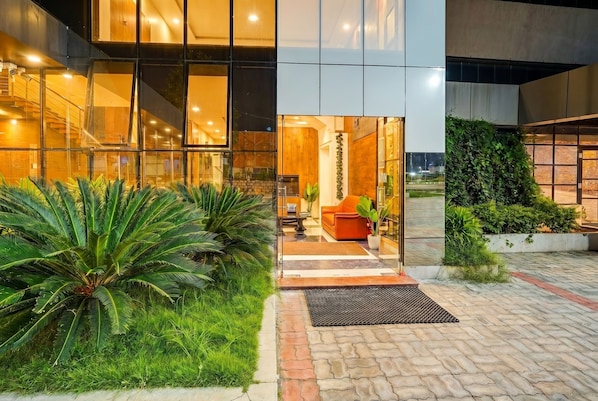 A modern building with a glass facade, a paved entrance area, and a seating area with a sofa and plants.