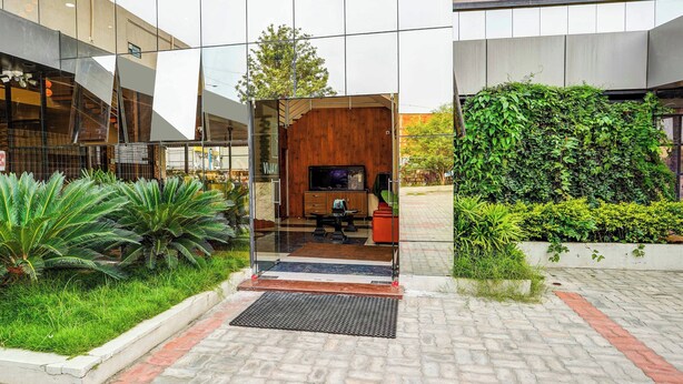 Edifício moderno com entrada de vidro, interior em madeira e área de jardim com diversas plantas.