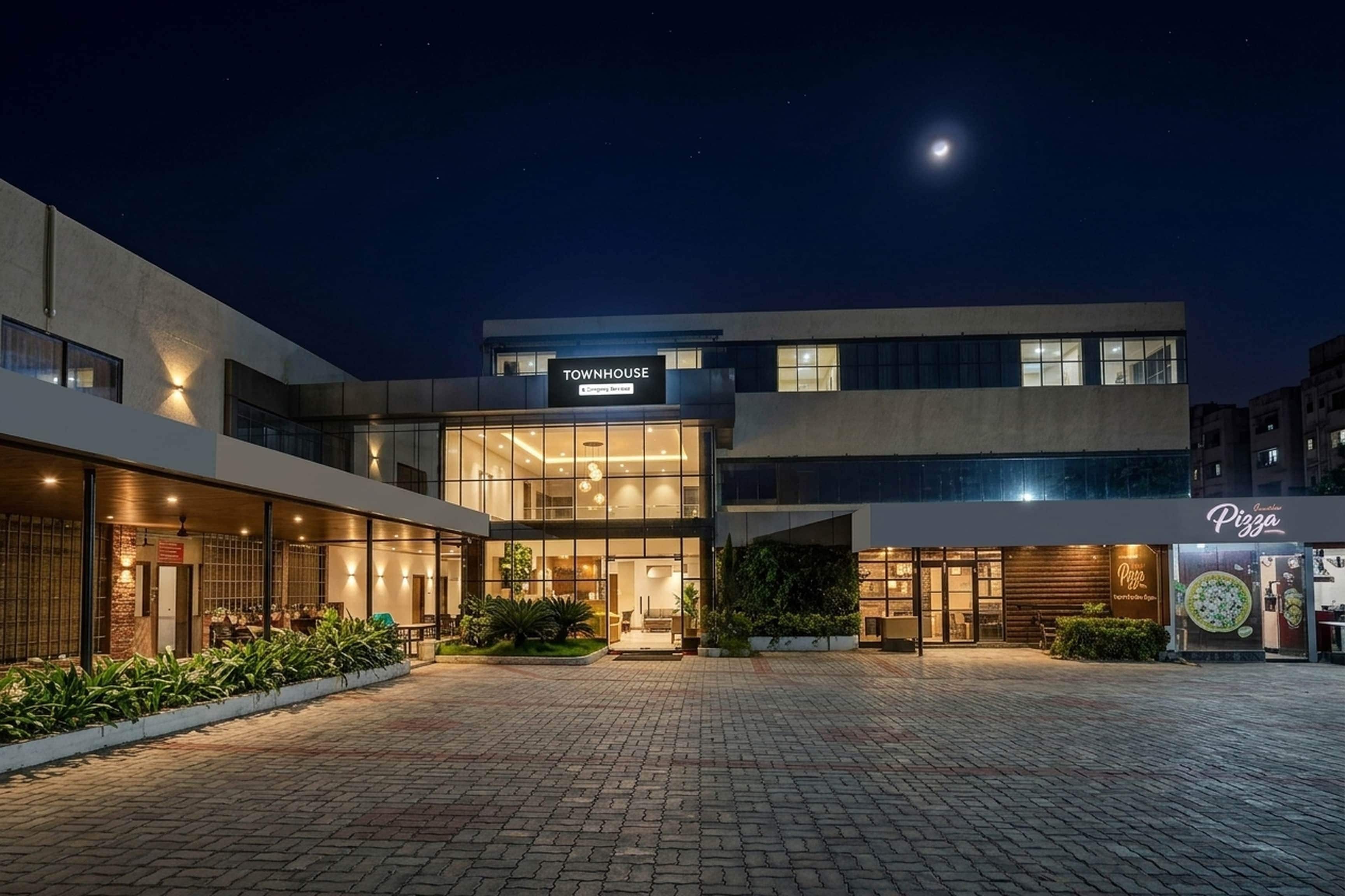 A modern townhouse with a well-lit entrance, a visible sign for a pizza restaurant, and a paved courtyard.